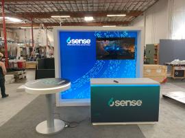 RENTAL: Modified RE-1081 Inline Design with White Laminated Framed Lightbox, Large Monitor Mount, 55" Monitor, RE-704 Charging Station Table, RE-1577 White Laminated Reception Counter, SEG Fabric Graphic, and Vinyl Applied Graphics